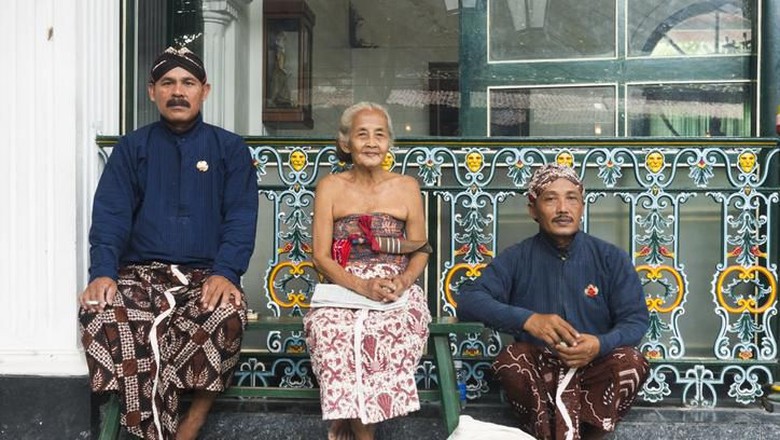 473672654 Yogyakarta, Indonesia - April 6, 2015: Three Javanese people wearing traditional clothing sit outside during a break while working at the Sultans Palace in Java, which is also called the Kraton. The two men wear head cloths and sarongs. The senior woman who sits in the middle wears a light colored sarong.
