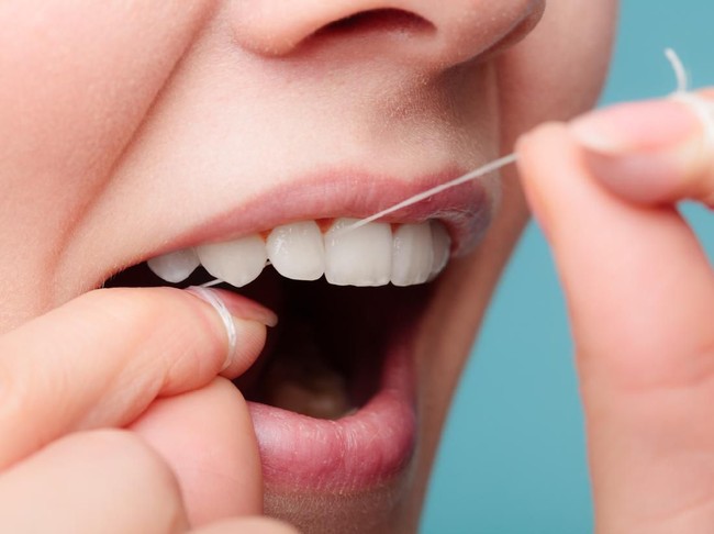 Portrait of a beautiful young woman flossing her teeth in the bathroom at home