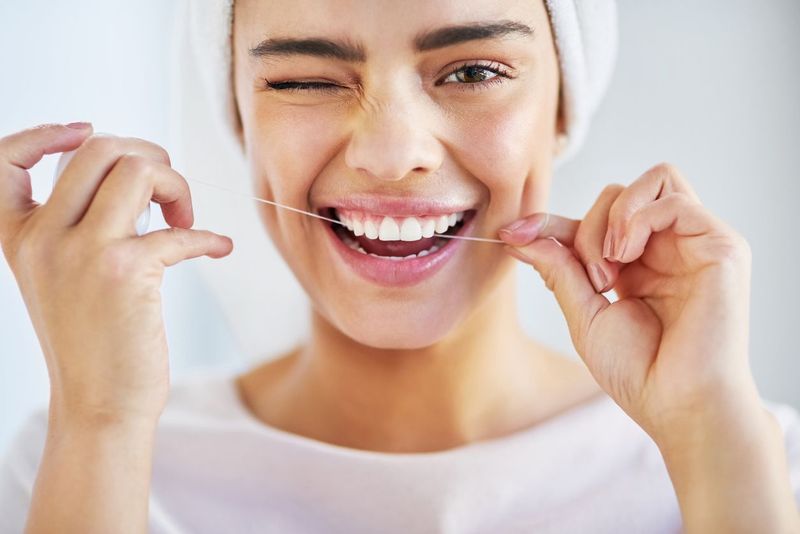 benang gigi Portrait of a beautiful young woman flossing her teeth in the bathroom at home