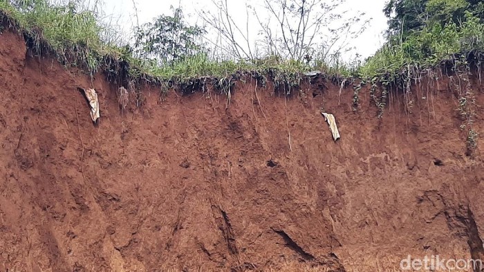 Longsor terjadi di TPU Kampung Nangerang, Kelurahan Ranggamekar, Kota Bogor. Tanah yang tergerus air membuat kain kafan menggelantung.