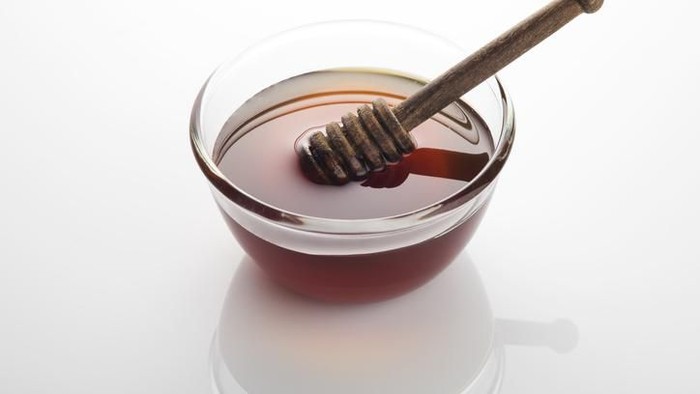 High resolution image of organic forest honey in a glass bowl with wooden honey dipper shot in studio on white background