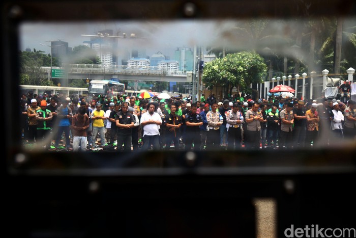 Massa pengemudi ojek online (ojol) gelar aksi unjuk rasa di depan Gedung DPR. Mereka pun turut melaksanakan Salat Jumat di kawasan tersebut.
