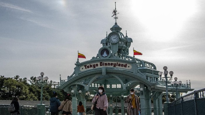 TOKYO, JAPAN - FEBRUARY 28: People pass beneath an archway leading to Tokyo Disneyland on the day it announced it will close until March 15th because of concerns over the Covid-19 virus, on February 28, 2020 in Tokyo, Japan. A growing number of events and sporting fixtures are being cancelled or postponed around Japan while some businesses are closing or asking their employees or work from home. Prime Minister Abe has also asked schools to close for around a month as Covid-19 cases continue to increase and concerns mount over the possibility that the outbreak will force the postponement or even cancellation of the Tokyo Olympics. (Photo by Carl Court/Getty Images)