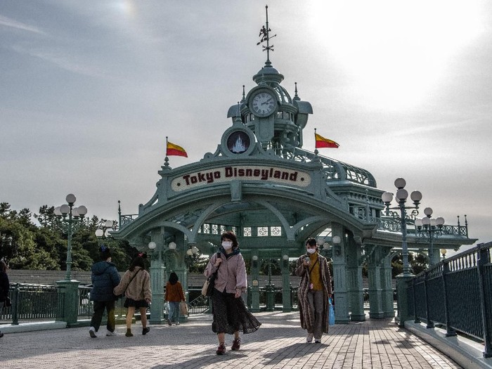 TOKYO, JAPAN - FEBRUARY 28: People pass beneath an archway leading to Tokyo Disneyland on the day it announced it will close until March 15th because of concerns over the Covid-19 virus, on February 28, 2020 in Tokyo, Japan. A growing number of events and sporting fixtures are being cancelled or postponed around Japan while some businesses are closing or asking their employees or work from home. Prime Minister Abe has also asked schools to close for around a month as Covid-19 cases continue to increase and concerns mount over the possibility that the outbreak will force the postponement or even cancellation of the Tokyo Olympics. (Photo by Carl Court/Getty Images)