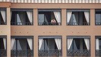 Seorang tamu hotel berdiri di balkon kamar sembari melihat pemandangan saat harus menjalani proses karantina terkait virus corona.
