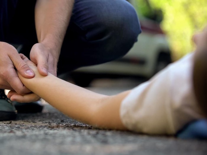 Man holding hand of girl lying on road, unconscious victim of car accident, 911