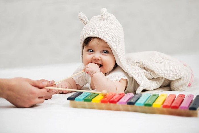 nama bayi Happy little kid, baby girl in 1 year plays a musical instrument xylophone in game center, of the childrens room for birthday or home.