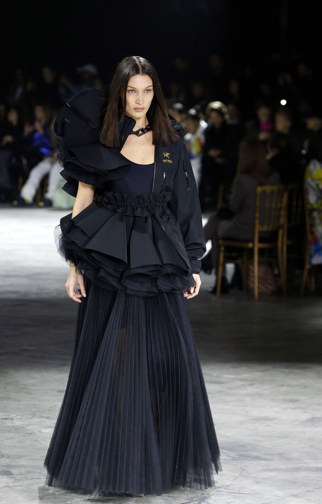 Bella Hadid, adik Gigi, menebar pesonanya dengan gaun hitam dengan peplum ruffle yang tak kalah dramatis. Dekorasi ruffle juga kembali hadir di bagian pundak jaket yang membungkus gaun tersebut. Foto: Getty Images/Thierry Chesnot