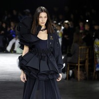 Bella Hadid, adik Gigi, menebar pesonanya dengan gaun hitam dengan peplum ruffle yang tak kalah dramatis. Dekorasi ruffle juga kembali hadir di bagian pundak jaket yang membungkus gaun tersebut. Foto: Getty Images/Thierry Chesnot