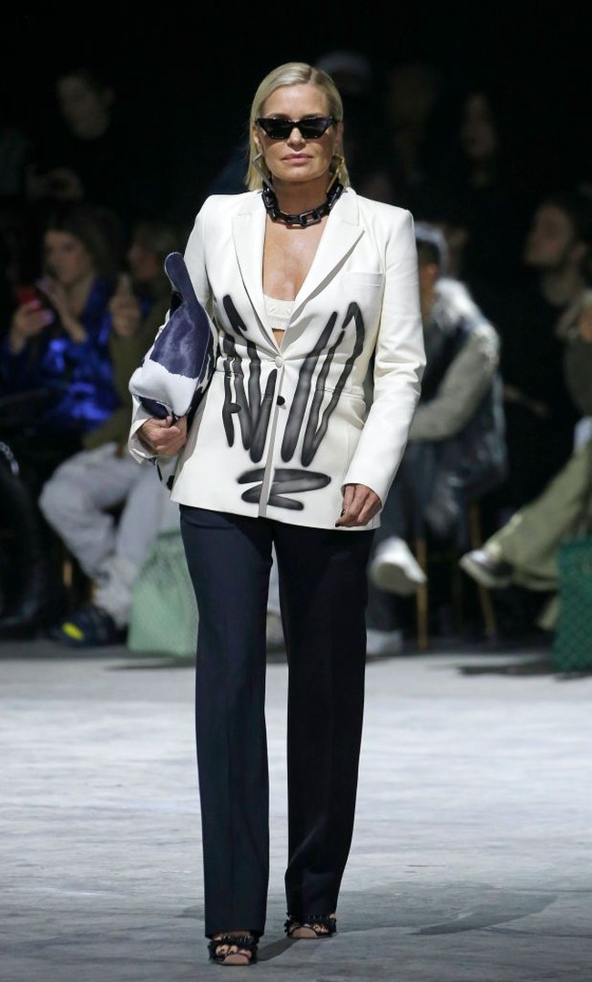 Kejutan datang ketika Yolanda Hadid yang bukan lain adalah ibunda Gigi dan Bella Hadid muncul di catwalk. Perempuan 56 tahun itu menunjukkan sisi hypebeast-nya dengan setelan yang blazernya dihiasi tulisan bergaya grafiti. Tidak ketinggalan kacamata hitam bergaya vintage. Foto: Getty Images/Thierry Chesnot