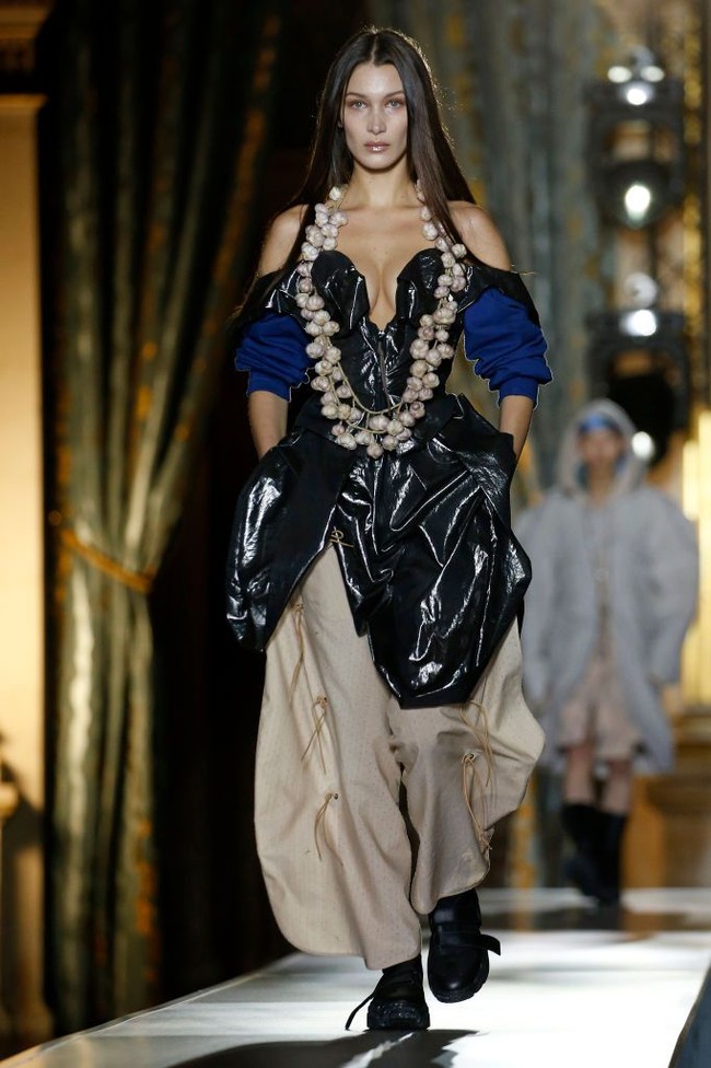 Di fashion show yang berlangsung di Hôtel de Ville yang megah dengan desain bergaya baroque-nya, Bella Hadid memeragakan dua look atau tampilan busana. Look pertama terdiri dari gaun off-shoulder seksi berwarna hitam yang dipadu dengan celana maxi coklat serta sneakers hitam. (Foto: Getty Images/Thierry Chesnot)