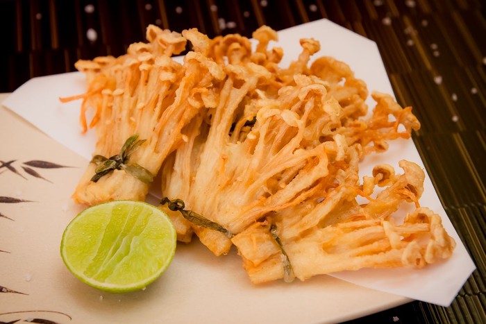 deep fried golden brown crispy Japanese enokitake needle shape mushroom with lime on black background