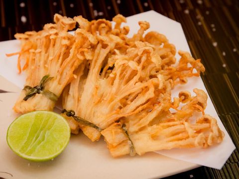 deep fried golden brown crispy Japanese enokitake needle shape mushroom with lime on black background
