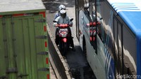Seorang pemotor menyempil di samping bus TransJakarta.