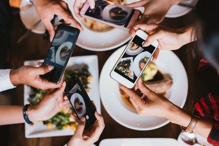 Close up focus view of hand and mobile while taking a photo of food on the plate in a restaurant for social media.