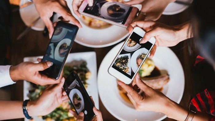 Close up focus view of hand and mobile while taking a photo of food on the plate in a restaurant for social media.