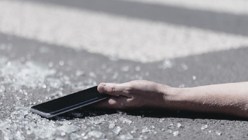 Close-up of a hand holding a mobile phone. Pieces of glass on the street