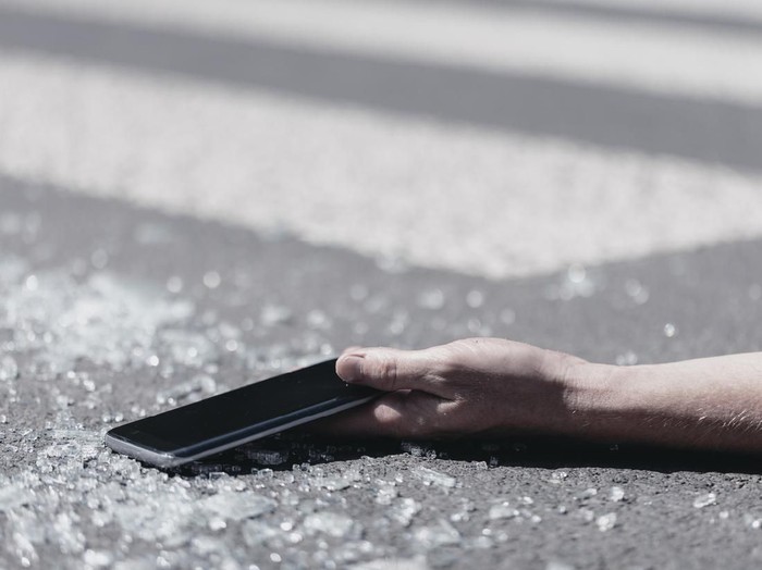 Close-up of a hand holding a mobile phone. Pieces of glass on the street