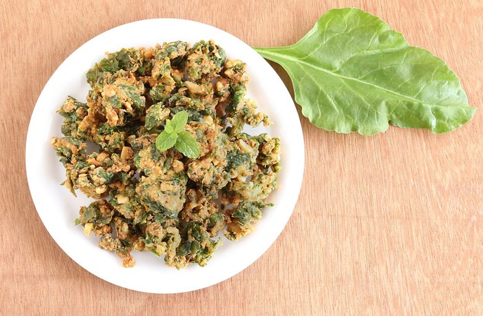 Palak pakoda, an Indian popular snack, on a plate, and palak or spinach leaf on a wooden background.