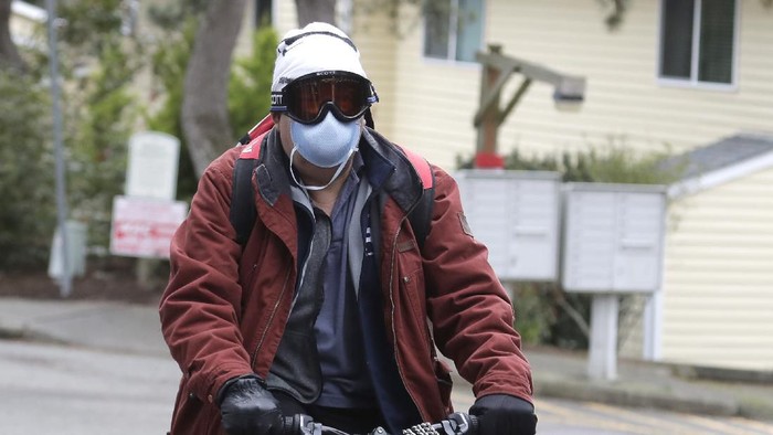 A man wearing a mask and goggles rides his bike out of the parking lot at the Life Care Center is shown in Kirkland, Wash., near Seattle, Tuesday, March 3, 2020. The facility has been tied to several confirmed cases of the COVID-19 coronavirus. (AP Photo/Ted S. Warren)