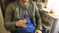 Segelas minuman menemani perjalanan Raphael menggunakan pesawat terbang. Ia duduk santai sambil memegang gelas. Foto: instagram @raphaelmaitimo
