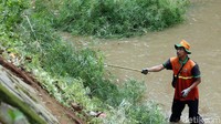 seorang petugas terlihat menggunakan Bambu untuk membersihkan rumput liar di dinding kali. Rengga Sancaya