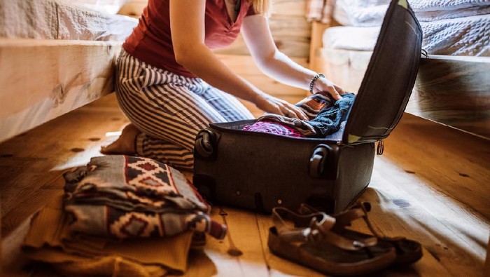 Unrecognizable woman packing luggage in log cabin, sitting on floor