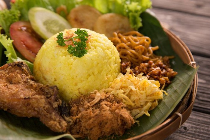 sarapan dari kunyit nasi kuning. indonesian yellow rice served with fried chicken on banana leaf