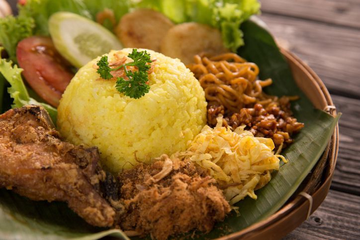 nasi kuning. indonesian yellow rice served with fried chicken on banana leaf