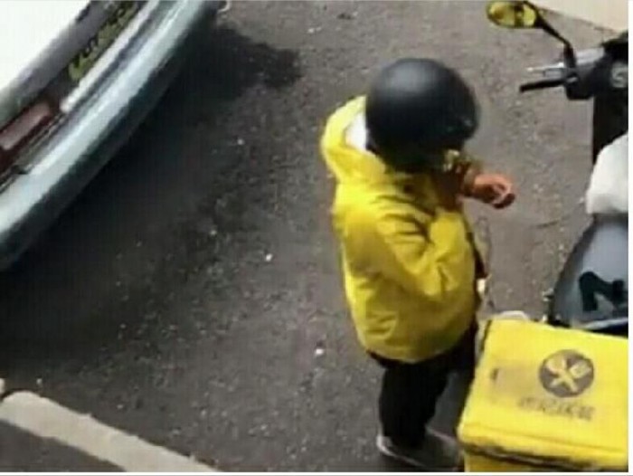 Young male courier in yellow sweatshirt delivering pizza, standing with thermal backpack and smart phone on the steret outdoors