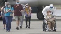 Seorang petuugas medis dengan menggunakan pakaian pelindung dan masker membantu mendorong kursi roda seorang penumpang kapal pesiar Grand Princess yang akan diterbangkan ke lokasi karantina. AP Photo/Jeff Chiu.