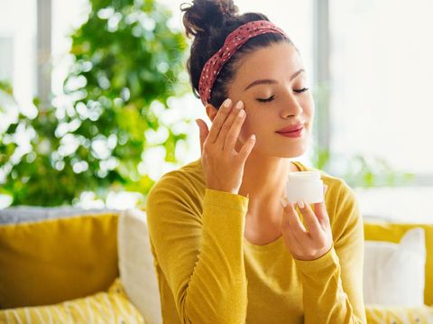 Young woman with eyes closed applying face cream.