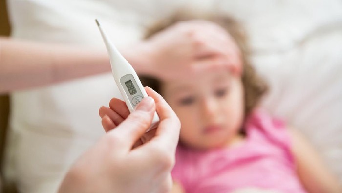 612409562 Close-up thermometer. Mother measuring temperature of her ill kid. Sick child with high fever laying in bed and mother holding thermometer. Hand on forehead.