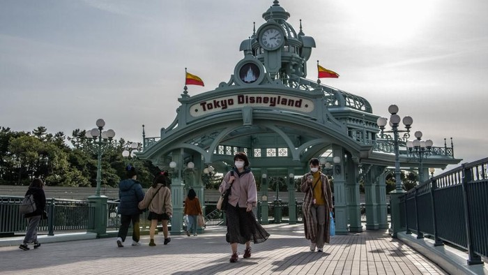 TOKYO, JAPAN - FEBRUARY 28: People pass beneath an archway leading to Tokyo Disneyland on the day it announced it will close until March 15th because of concerns over the Covid-19 virus, on February 28, 2020 in Tokyo, Japan. A growing number of events and sporting fixtures are being cancelled or postponed around Japan while some businesses are closing or asking their employees or work from home. Prime Minister Abe has also asked schools to close for around a month as Covid-19 cases continue to increase and concerns mount over the possibility that the outbreak will force the postponement or even cancellation of the Tokyo Olympics. (Photo by Carl Court/Getty Images)