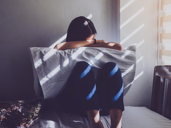 wanita sedih Asian women are sitting hugging their knees in bed. Feeling sad, disappointed in love In the dark bedroom and sunlight from the window through the blinds.Vintage tone.
