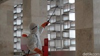 Petugas dengan mengenakan jas hazmat, masker serta kacamata menyemprotkan disinfektan di dinding-dinding masjid.