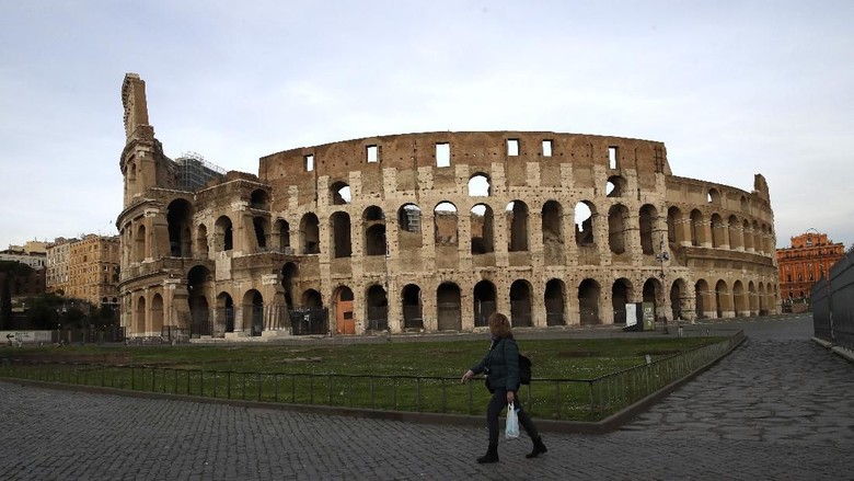 Situasi di sekitar Colosseum di Roma cenderung sepi saat lockdown diberlakukan untuk mencegah penyebaran virus Corona A woman walks in front of Romes ancient Colosseum in the afternoon of Thursday, March 12, 2020. A sweeping lockdown is in place in Italy to try to prevent it from becoming the next epicenter of the coronavirus epidemic. For most people, the new coronavirus causes only mild or moderate symptoms. For some, it can cause more severe illness, especially in older adults and people with existing health problems. (AP Photo/Alessandra Tarantino)