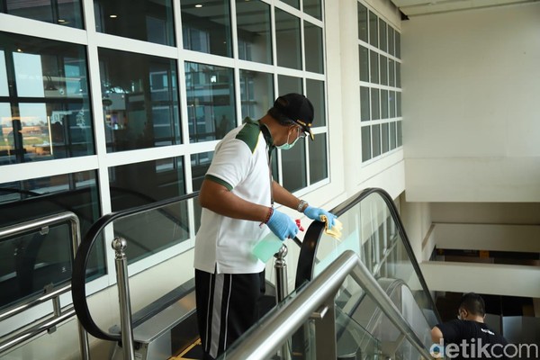 AP I Bandara I Gusti Ngurah Rai melakukan pembersihan dengan disinfektan di fasilitas terminal penumpang. Seorang petugas membersihkan pegangan eskalator (Foto: Angga Riza/detikcom)