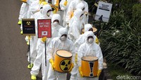 Para peserta aksi tampak mengenakan jas hazmat atau pakaian pelindung khusus serta masker saat ikut serta dalam aksi tolak nuklir tersebut.