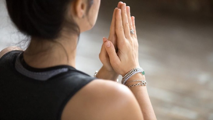 Namaste gesture close up photo, young attractive woman practicing yoga, working out, wearing wrist bracelets and rings, indoor, yoga studio, behind the shoulder view. Contemplation concept