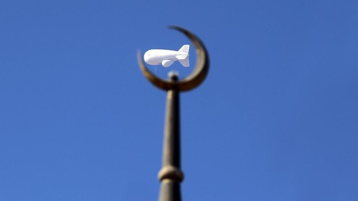 A picture taken on October 5, 2013 in Kuwait City shows a military balloon flying above a crescent on the top of a mosque. The observation baloon, that contains radars and electronic intelligence systems, is used  by the Kuwaiti Ministry of Defense in north Kuwait to monitor the borders or for metereology purposes as well.   AFP PHOTO YASSER AL-ZAYYAT (Photo by YASSER AL-ZAYYAT / AFP)
