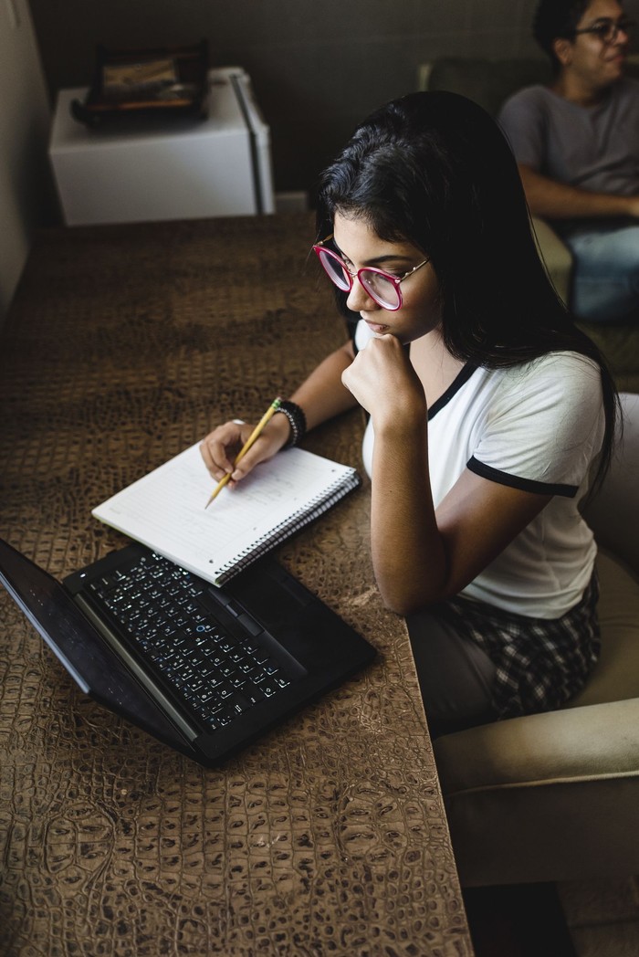 Teenage girl studying and drinking juice sitting on sofa at home