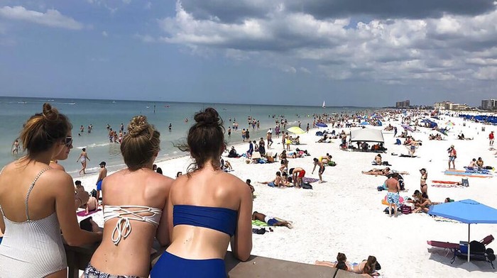 In this photo provided by Sarah J. Hollenbeck, people gather at Clearwater Beach in Florida, Monday, March 16, 2020. Amid coronavirus concerns, the governor has left it to local communities to decide if they would restrict access to beaches. (Sarah J. Hollenbeck via AP)