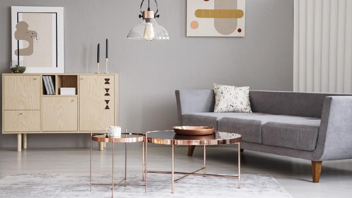Abstract paintings on a gray wall of a classy living room interior with a wooden sideboard and shiny golden coffee tables