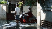 Seorang warga menerobos genangan air saat melintasi kawasan permukiman di Jakarta Timur.