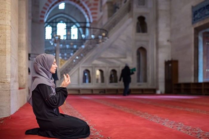Muslim woman in headscarf and hijab prays with her hands up in air in mosque.Religion praying concept.
