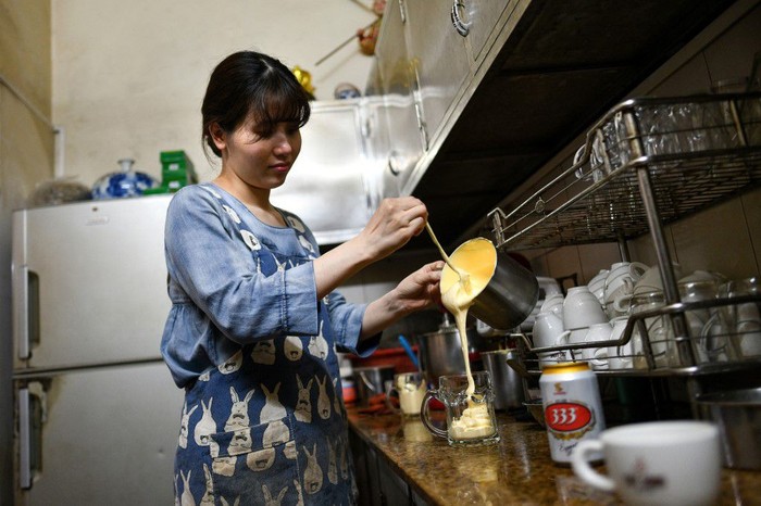 This picture taken on April 4, 2019 shows Nguyen Giang, daughter of Giang Cafe owner Nguyen Chi Hoa, pouring a sweetened egg mixture into a beer mug at the decades-old cafe in Hanoi. - Scrambled, fried, or ... whipped into beer? It might not be the most conventional way to serve eggs, but a decades-old Hanoi cafe is delighting drinkers with a frothy beer cocktail that has no place on a breakfast menu. (Photo by Manan VATSYAYANA / AFP) / TO GO WITH STORY VIETNAM-LIFESTYLE-BEVERAGE-BEER,FOCUS