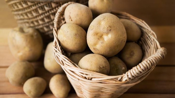 potatoes in a wicker basket on wood.