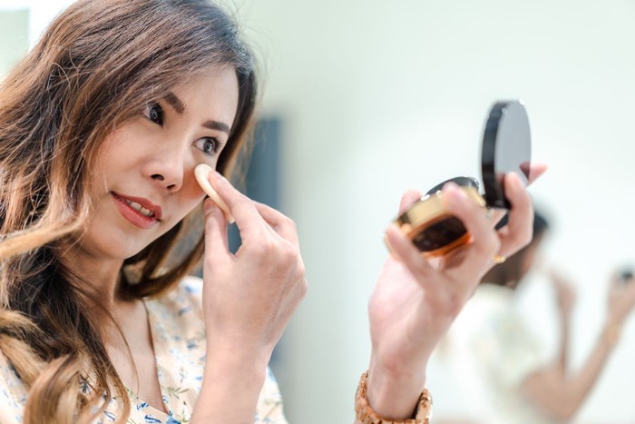 Portrait of Beautiful young Asian woman applying makeup, Attractive girl looking at mirror in pressed powder compact, holding make-up sponge. To cover face wrinkles, make skin smooth. Selective focus