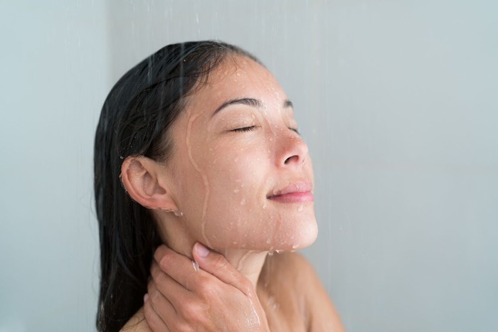 Mandi Air Panas Bunuh Virus Corona? Shower woman showering relaxing under water massaging neck in hot shower. Asian female adult face enjoying spa relaxation time relaxing meditating in warm bath cleaning face and body at home.